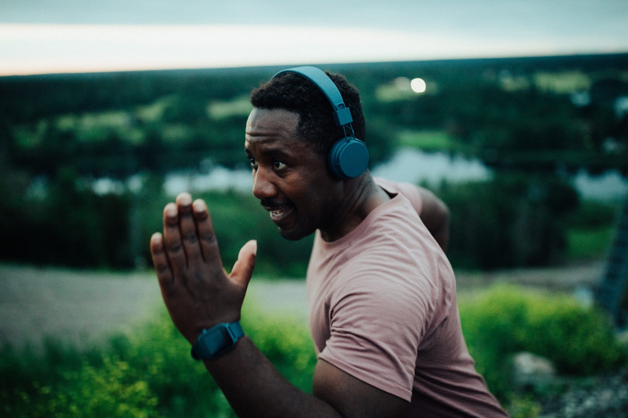 A man with headphones stretching on a hill above a lake
