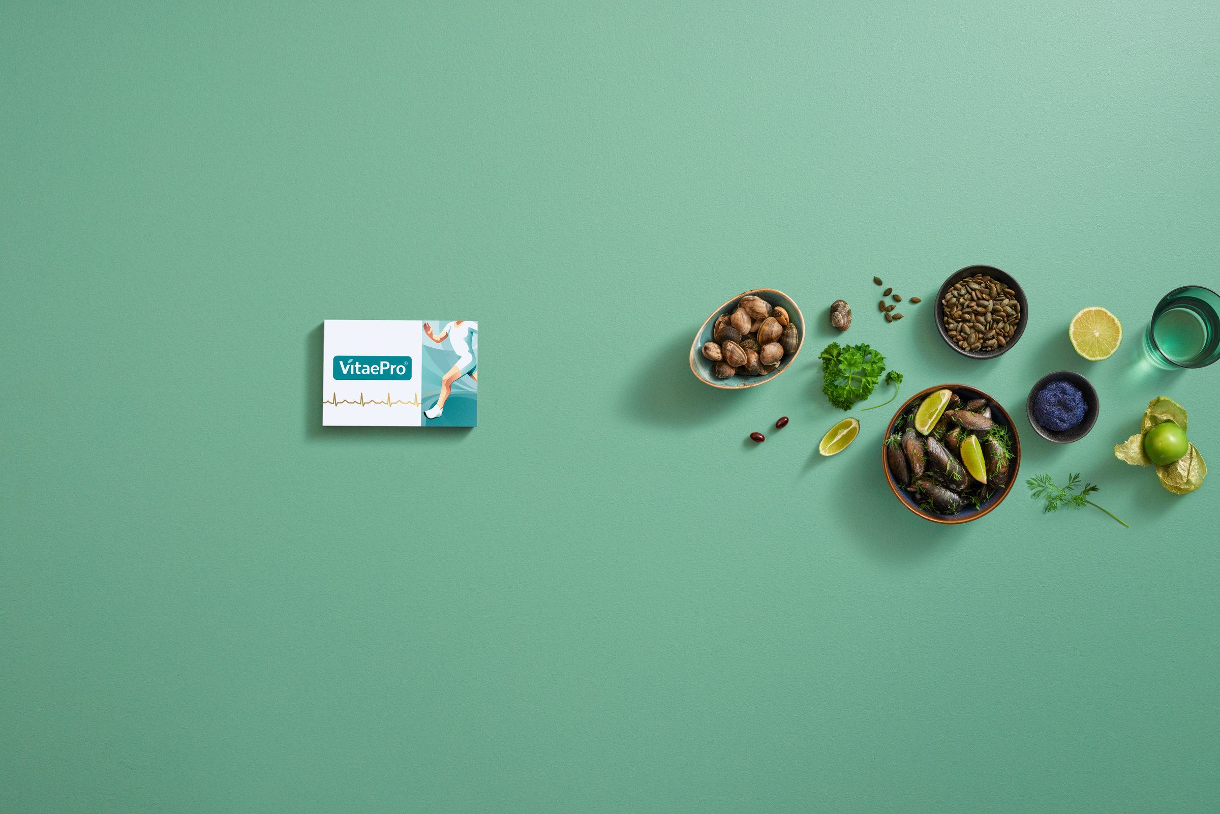 VitaePro pack on a sea green surface, with bowls of mussels, blueberries, a glass of water and herbs arranged to the right