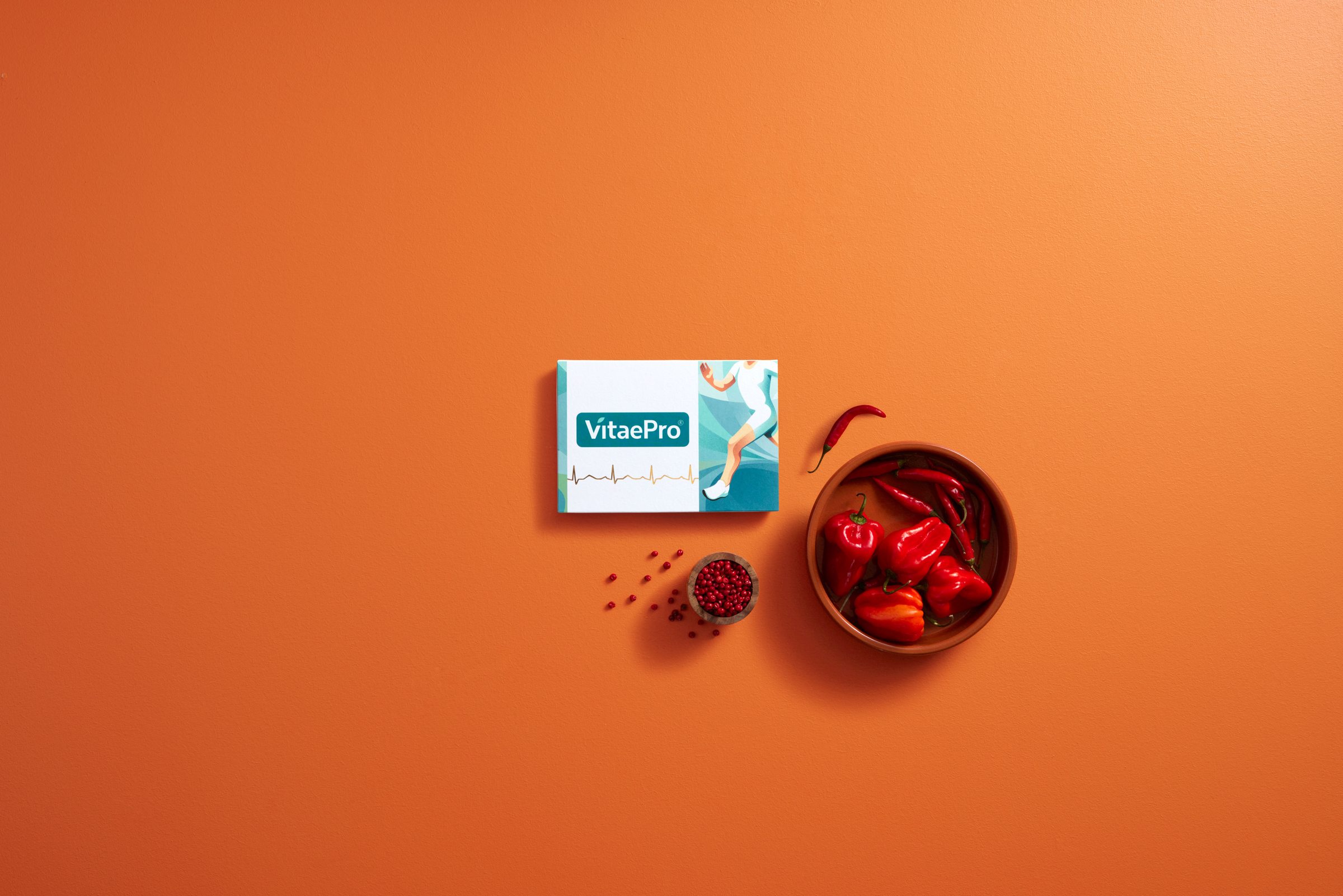 VitaePro pack, capsules and red peppers on an orange surface, from above