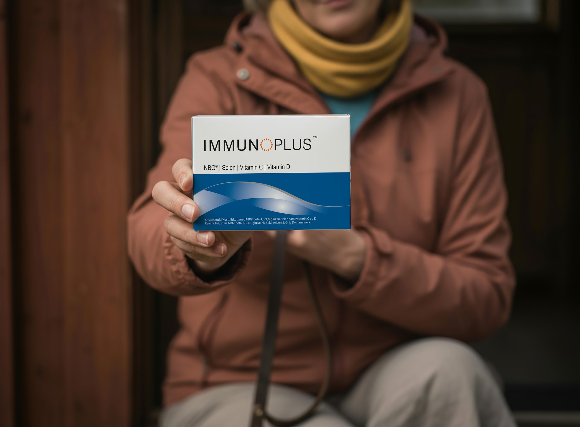 A person in an autumn jacket holding out an ImmunoPlus pack